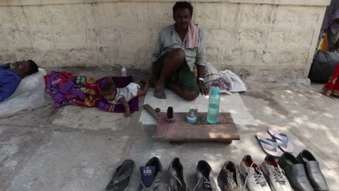 Cobbler baby sits while waiting for customers on sidewalk Stock Footage 95455653