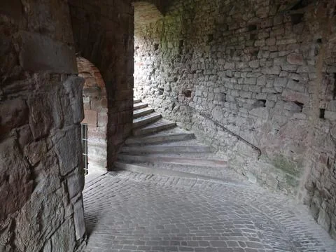 Cobblestone path leading to worn stone steps in a dimly lit castle passage,.. Foto stock