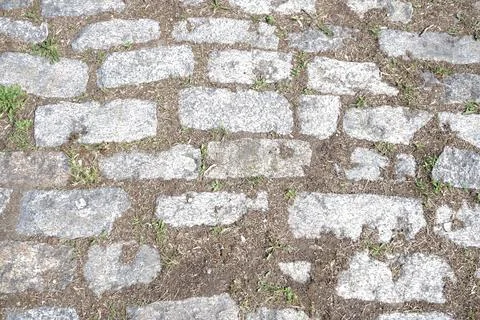 Cobblestone pavement texture with sparse grass and dirt in between stones Stock Photos
