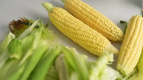 Cobs of fresh yellow corn with green leaves lie on kitchen table top view Vídeo Stock 201295308