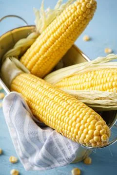 Cobs of ripe raw corn in basket on blue wooden background, close-up. Flat lay Stock Photos