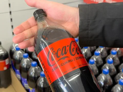 Coca-Cola bottle held in a hand at a retail store shelf displaying carbonated Stock Photos