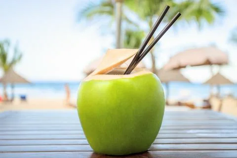 Coconut with cocktail drinking straw in front of tropical sea background Stock Photos