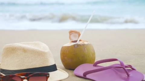 Coconut with drinking straw, hat, sunglasses and beach slippers on a sand at the Stock-Footage 62625081