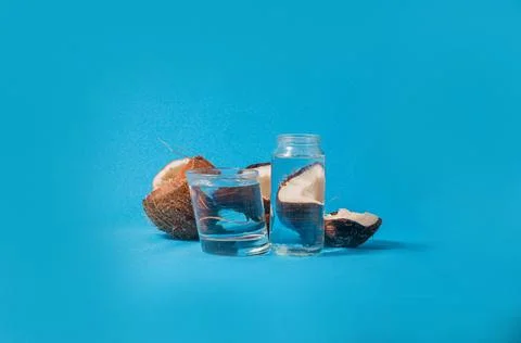 Coconut halves distorted through glasses with water. Blue background. Summer Stock Photos