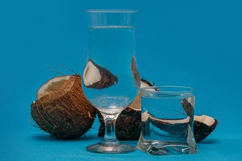 Coconut halves distorted through glasses with water. Blue background. Summer Stock Photos