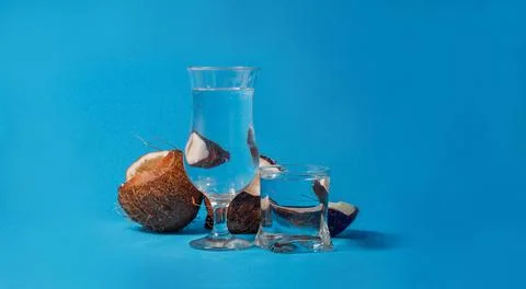 Coconut halves distorted through glasses with water. Blue background. Summer Stock Photos