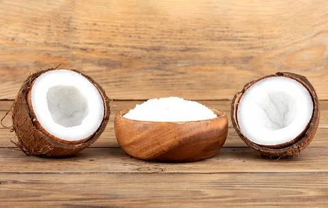 Coconut split in half and a bowl with coconut flakes on a wooden background. Stock Photos