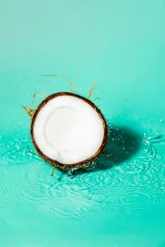 Coconuts cut in half with splashes on colourful background. Stock Photos