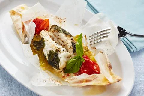 Cod cooked in parchment paper with tomatoes and herbs Stock Photos