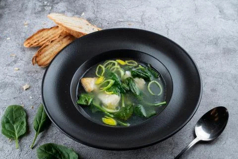 Cod ear soup with fresh spinach and cod pieces on stone background Stock Photos