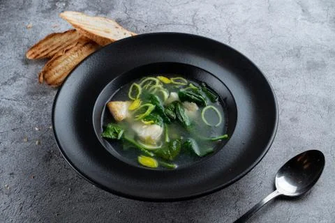 Cod ear soup with fresh spinach and cod pieces on stone background Stock Photos