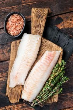 Cod fish fillets, raw codfish with thyme on wooden board. Wooden background.. Stock Photos