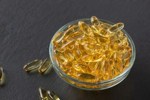 Cod liver fish oil capsules in glass bowl on black slate plate background. Close Stock Photos