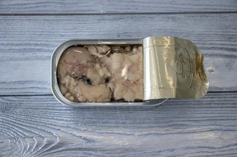 Cod liver in a tin on a gray background, flat top view. Stock Photos