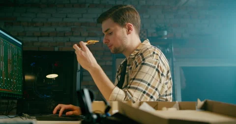 Coder Works at PC Eating Pizza in Loft Electronics Workshop or Home Garage Stock Footage 151846142