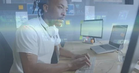 Coding Black man wearing white shirt and white headphones, typing at wooden desk 스톡 사진