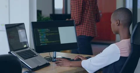 Coding female developer using laptop and external monitor in open-plan office, Foto stock