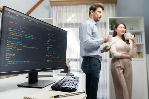 Coding screens on desk against developers drinking coffee standing. Postulate. Stock Photos