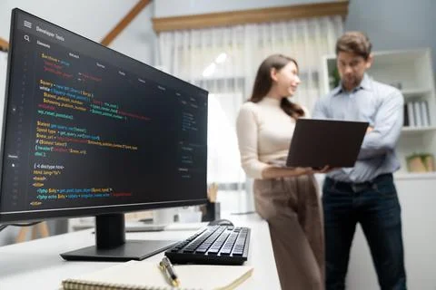 Coding screens on desk against developers working on laptop standing. Postulate. Stockfoto's