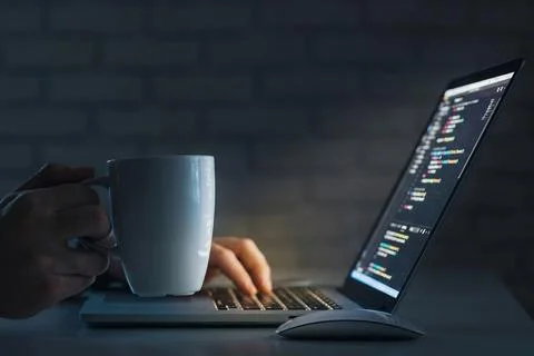 Coding session with coffee in a dimly lit room at night on a laptop Stock Photos