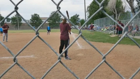 Coed softball batter get hit Runners score Viewed through back stop-Slow motion Stock Footage