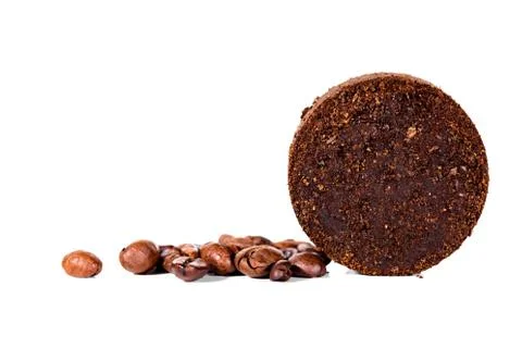 Coffee beans and round pressed coffee grounds in front of white 库存照片