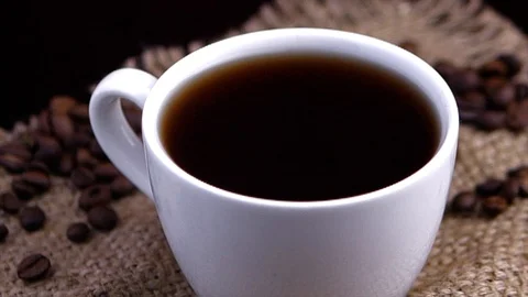 Coffee beans are lying around, close-up drops of coffee falling into a cup. Video stock 122057280
