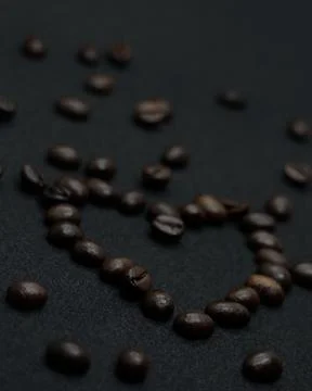 Coffee beans on a black background in the shape of a heart, view from the left Stock Photos