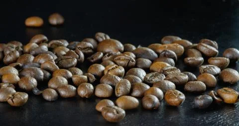 Coffee beans on a black surface, a large number, scattered, close-up, low key Stock Photos