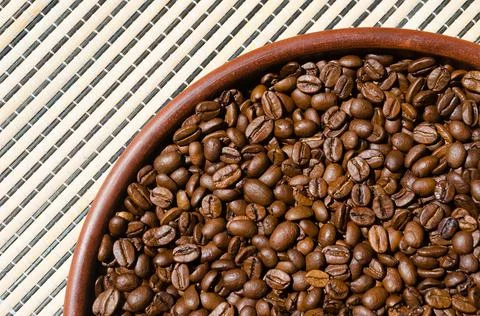 Coffee beans in a ceramic plate on the background of a wicker tablecloth. Stock Photos