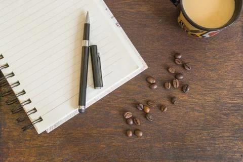 Coffee beans, cup of coffee, notebook on wooden deck Stock Photos