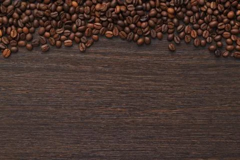 Coffee beans on a dark wooden table are located on top of the frame with the  Stock Photos