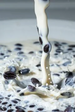 Coffee beans falling on the milk splash. Stock Photos