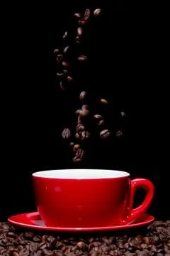Coffee beans falling into red coffee cup. Stock Photos