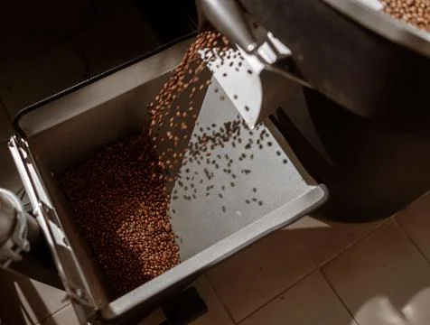 Coffee beans falling from release chute of coffee roaster machine Stock Photos