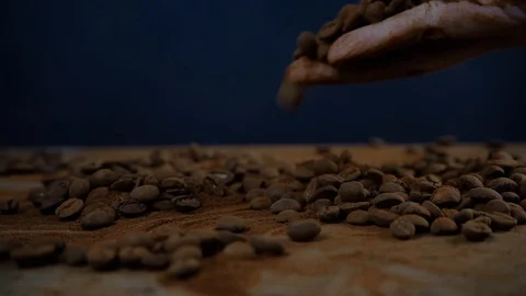 Coffee beans falling on a table on dark background, coffee in a hand slow motion Stock Footage 125401879