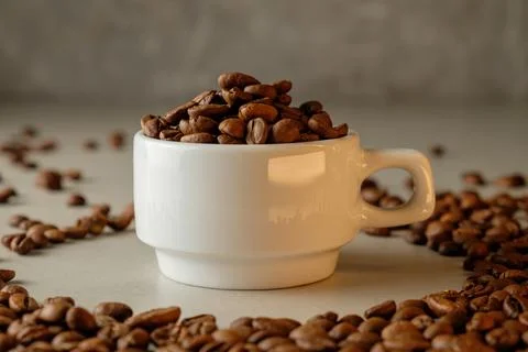 Coffee beans fill a cup while creating an aromatic tableau on a table Stock Photos