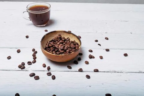 Coffee beans in front of cup of coffee on white planks Photos