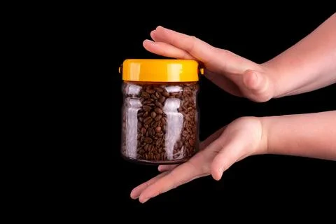 Coffee beans in the glass jar holding male hands. Isolated on black backgro.. Stock Photos