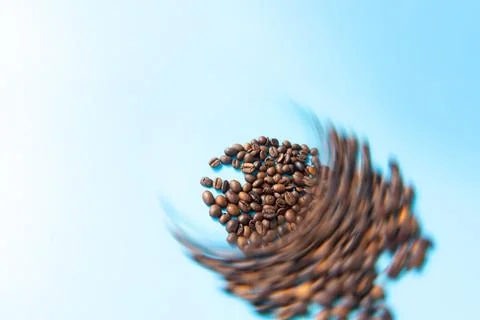 Coffee beans in motion on a light blue background, showcasing a dynamic swi.. Stock Photos