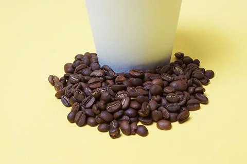 Coffee beans next to a paper cup on a white-yellow background Stock Photos