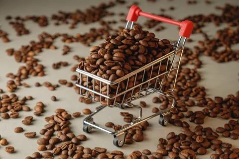 Coffee beans overflow from a tiny shopping cart on a textured surface Stock Photos