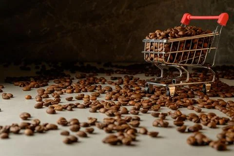 Coffee beans scattered around a tiny shopping cart in a warm setting Stock Photos