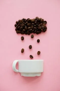 Coffee beans in shape of cloud pouring rain drops in a white cup on pink Stock Photos
