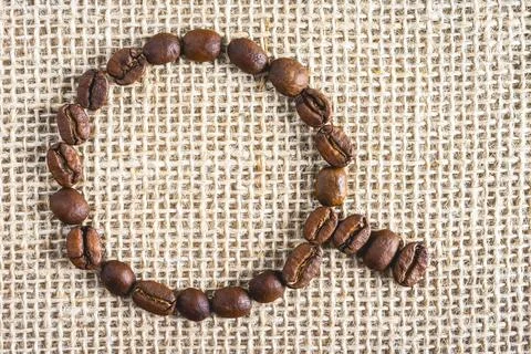 Coffee beans in the shape of a cup, on a burlap fabric. Stock Photos