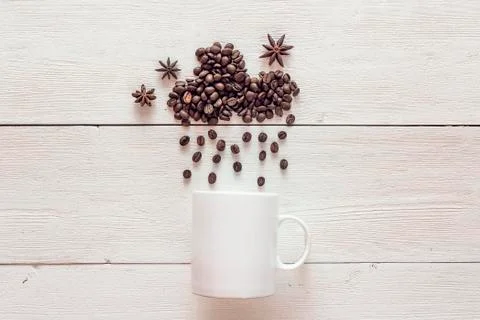 Coffee beans in shape of rainy cloud with anise stars and white cup on white  Stock Photos