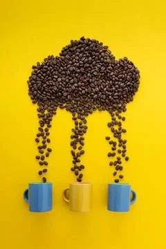 Coffee beans in shape of rainy cloud with three cups on yellow background. It Stock-Fotos