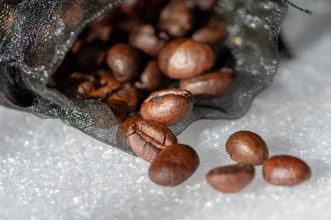 Coffee beans spilling from mesh bag onto textured white surface Stock Photos