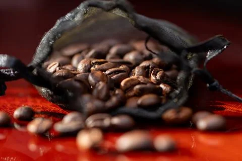 Coffee beans spilling from a small black mesh pouch Фото